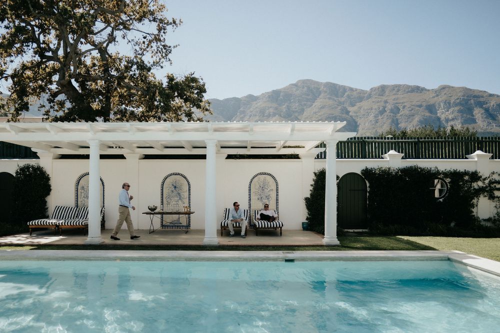 Elegant white pergola with arched details overlooking a swimming pool with mountains in the background.