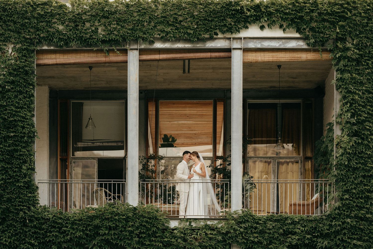 A figure in a white dress stands on an ivy-covered mansion's porch between elegant white columns.