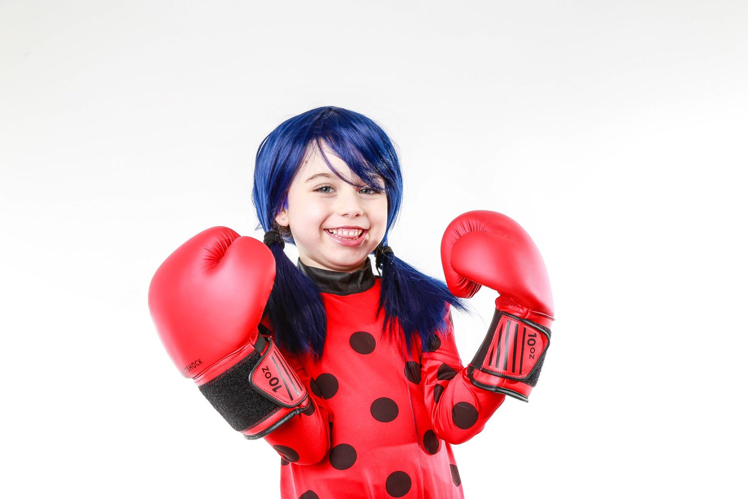 A person in a red polka dot outfit wearing red boxing gloves poses cheerfully against a white background.