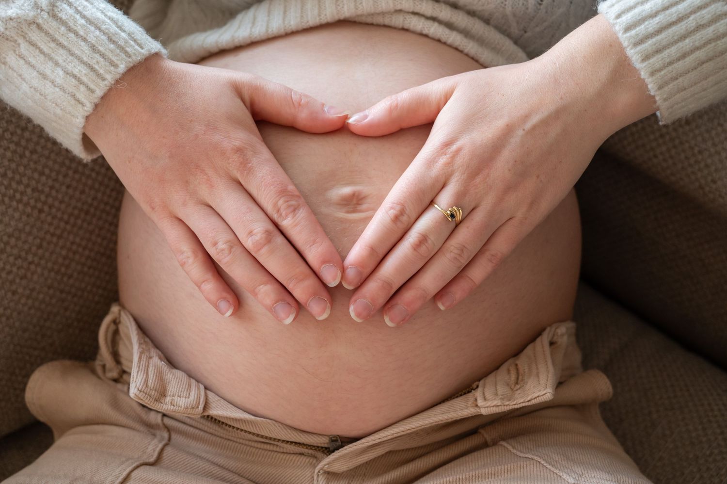 À Saint-Hubert, détail du ventre de la future maman avec les mains en forme de cœur lors d’une séance photo grossesse