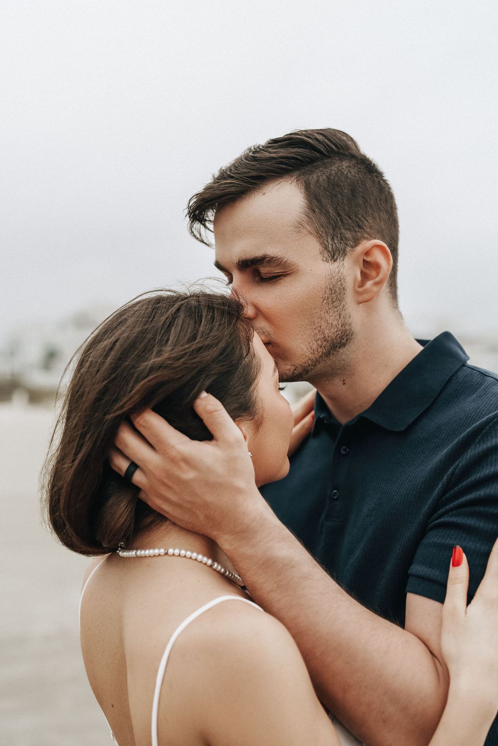 Intimate couple embraces in romantic kiss on cloudy beach.