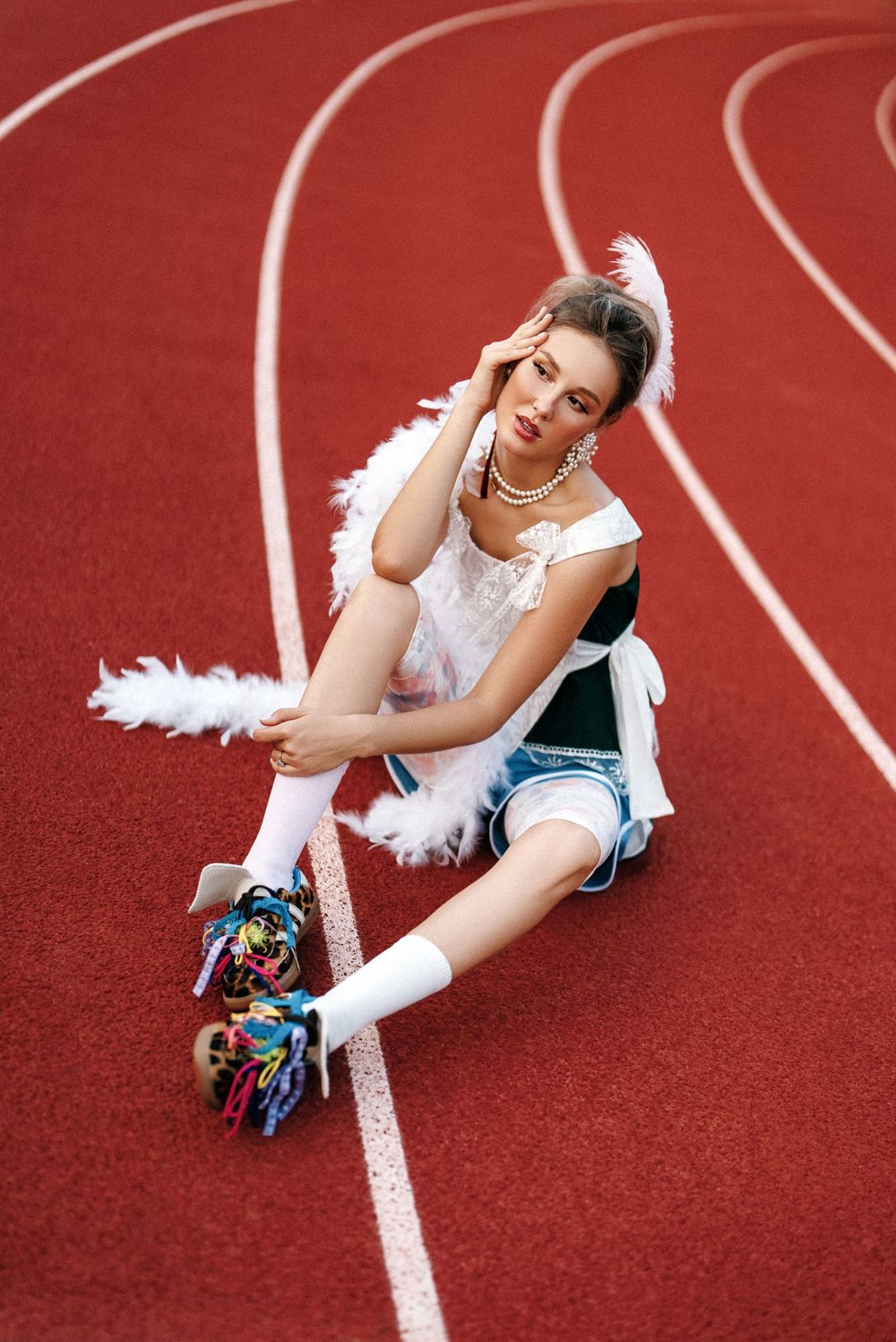 Playful dancer in white outfit with feathers poses on red running track.