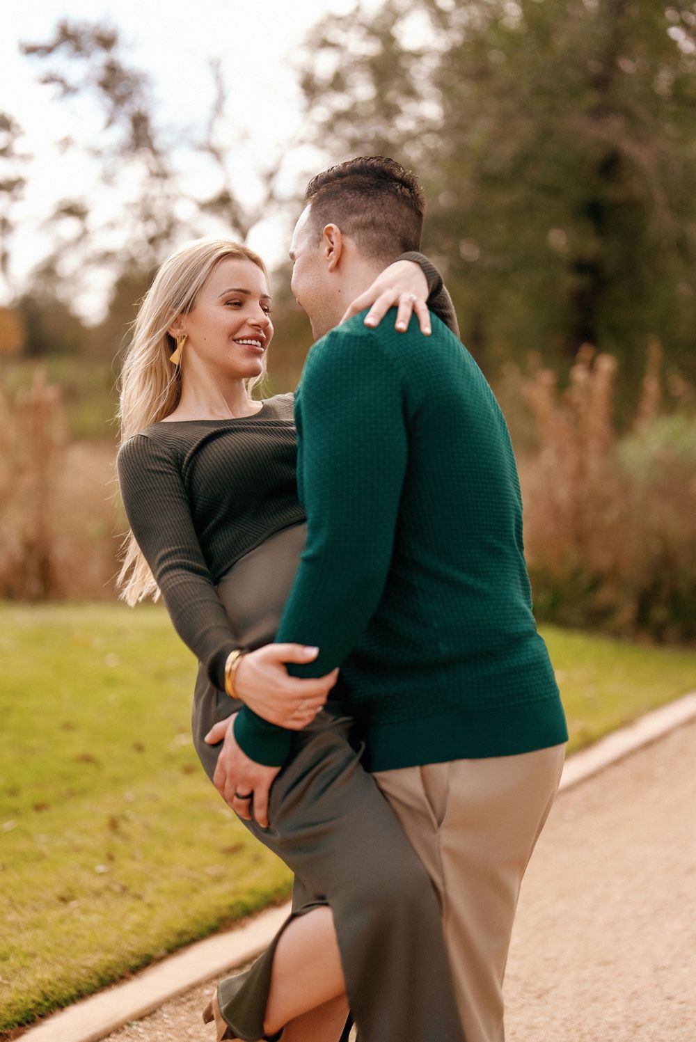 Couple embraces outdoors during maternity photoshoot in autumn setting.