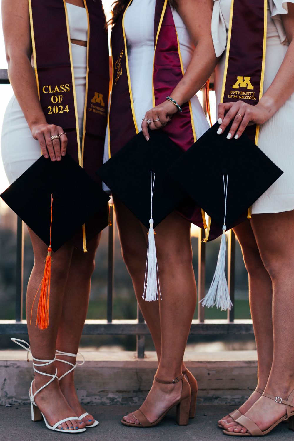 Close-up of graduates holding caps showing Class of 2024 stoles and formal footwear.