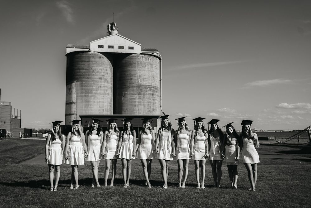 Black and white photo of graduates posing in line formation in front of grain silos.