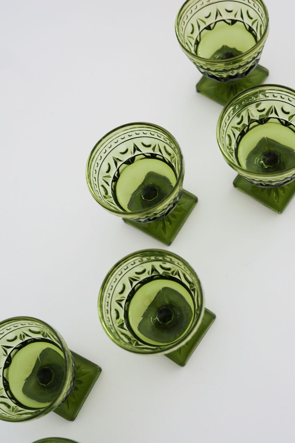 Vintage green glass teacups arranged in a diagonal line on white background.