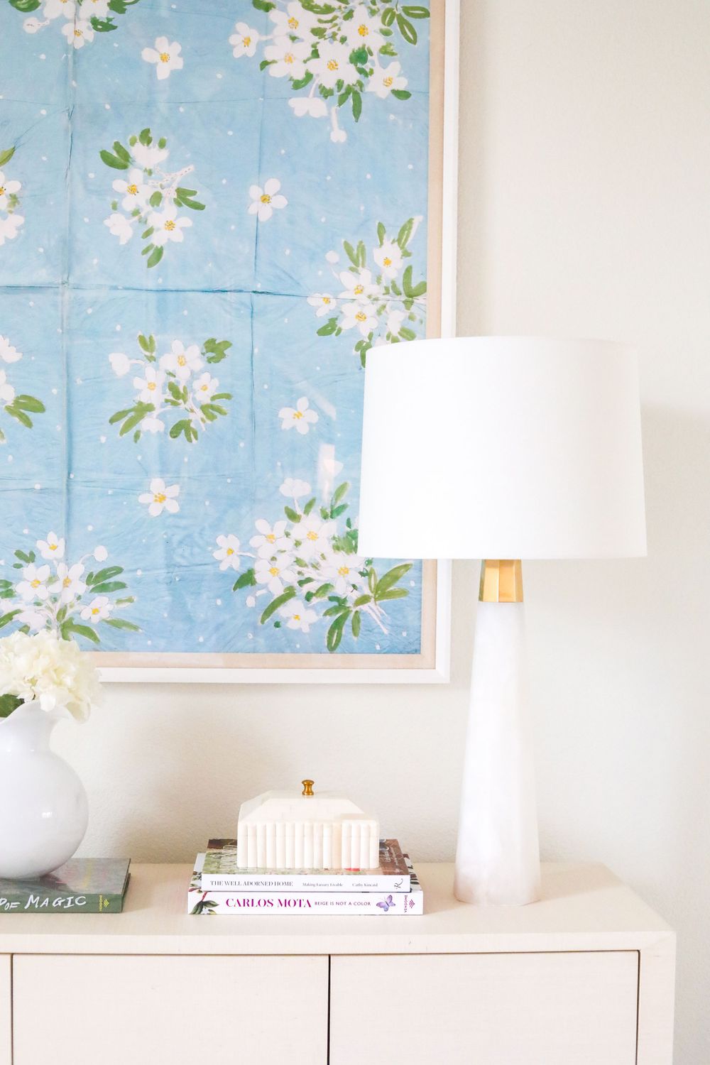 White credenza with table lamps and framed floral artwork in soft blue tones.