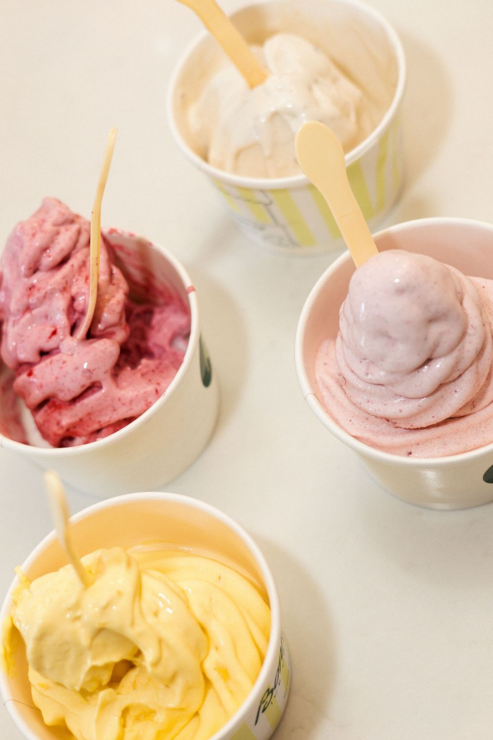 Various flavors of frozen yogurt in white cups including pink, yellow and white varieties.