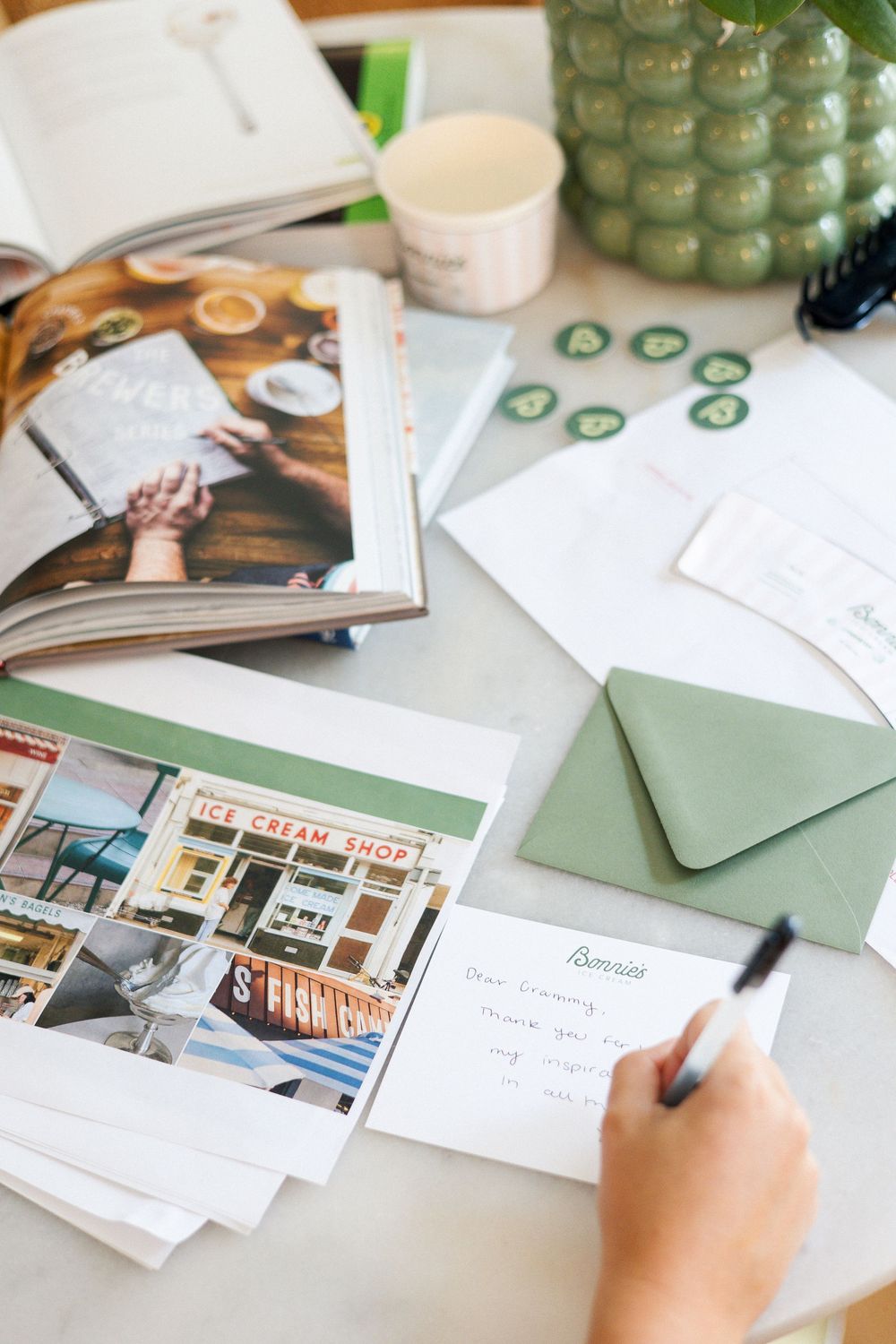 Wedding planning materials and photographs spread across a wooden desk with green accents.