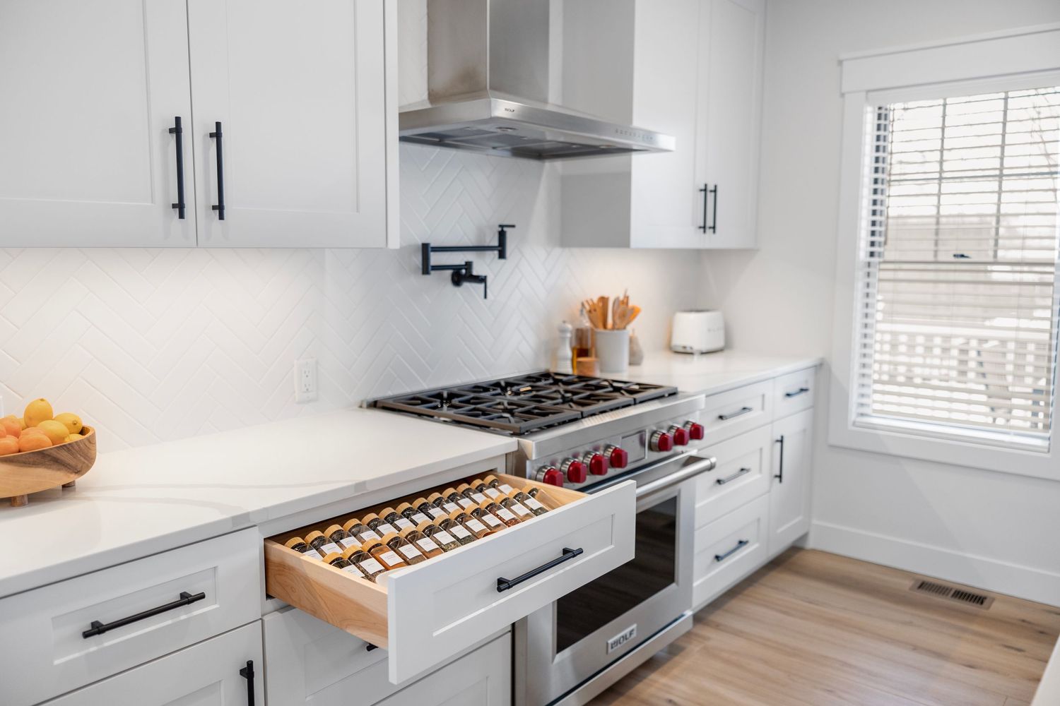 Modern white kitchen with gas range, pot filler, and custom spice drawer.