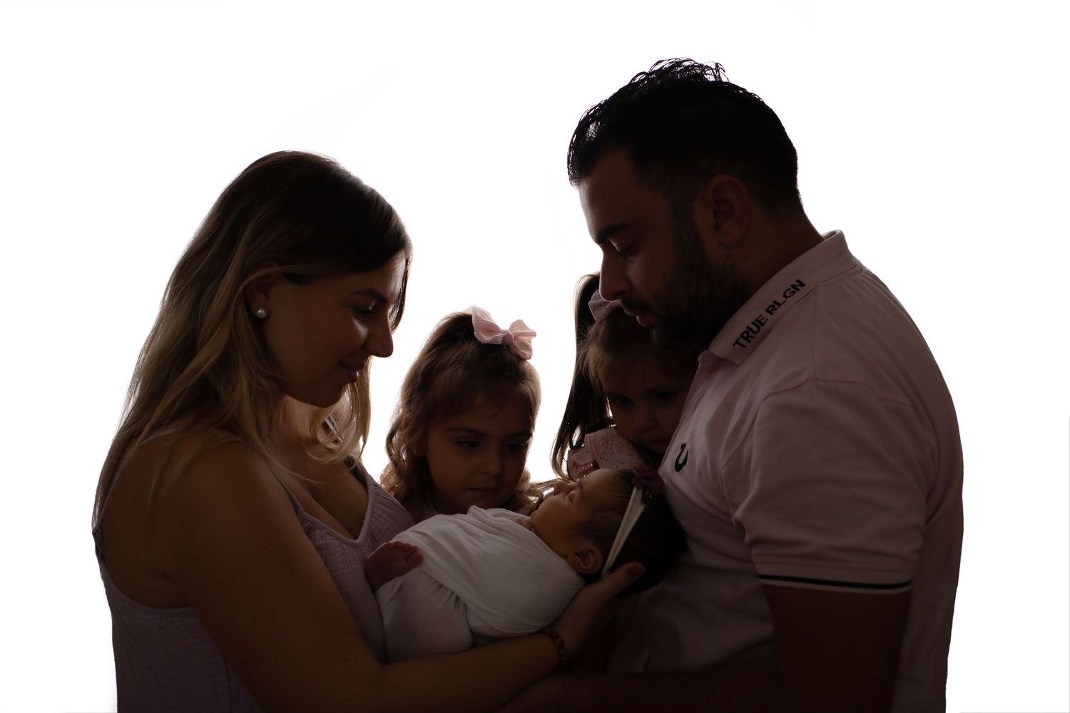 A silhouetted family sharing a tender moment as they gently hold their newborn baby together.