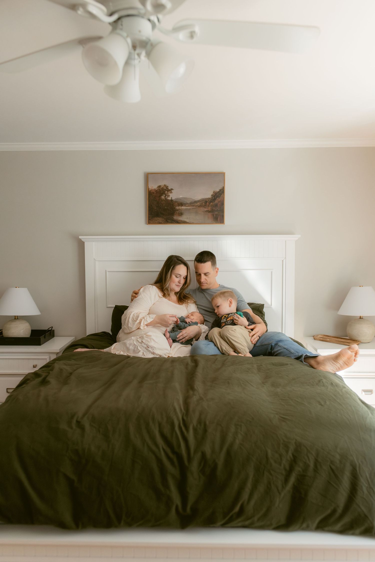 Round mirror reflection shows a cozy nursery interior with a ceiling fan and family gathering around a brown leather chair.