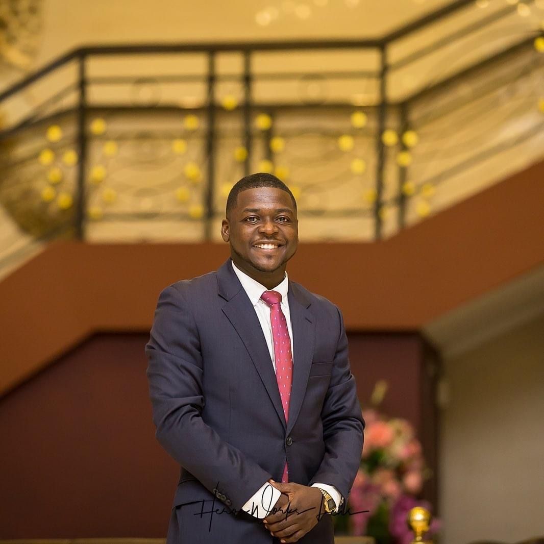 Professional in navy suit and red tie stands confidently in front of illuminated interior.