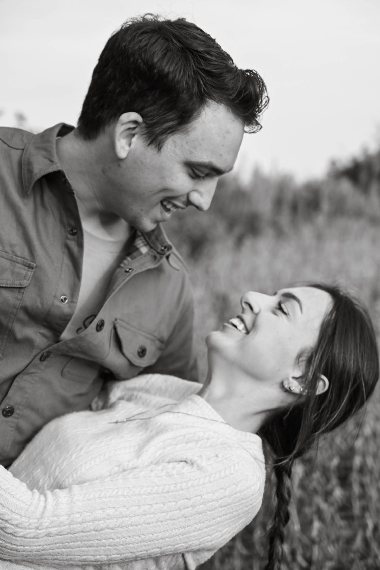 A candid black and white photo of a couple laughing together outdoors in a field.