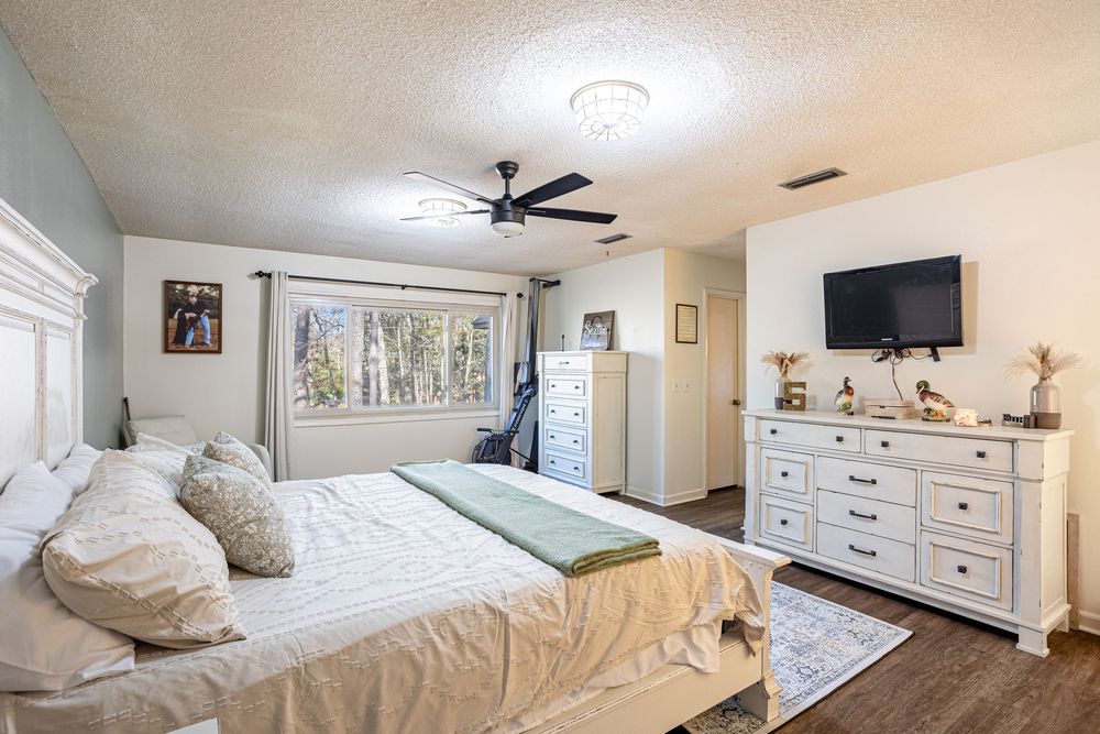 Cozy white bedroom interior with matching furniture set, dresser, mounted TV, and plush bedding in Dothan, AL.