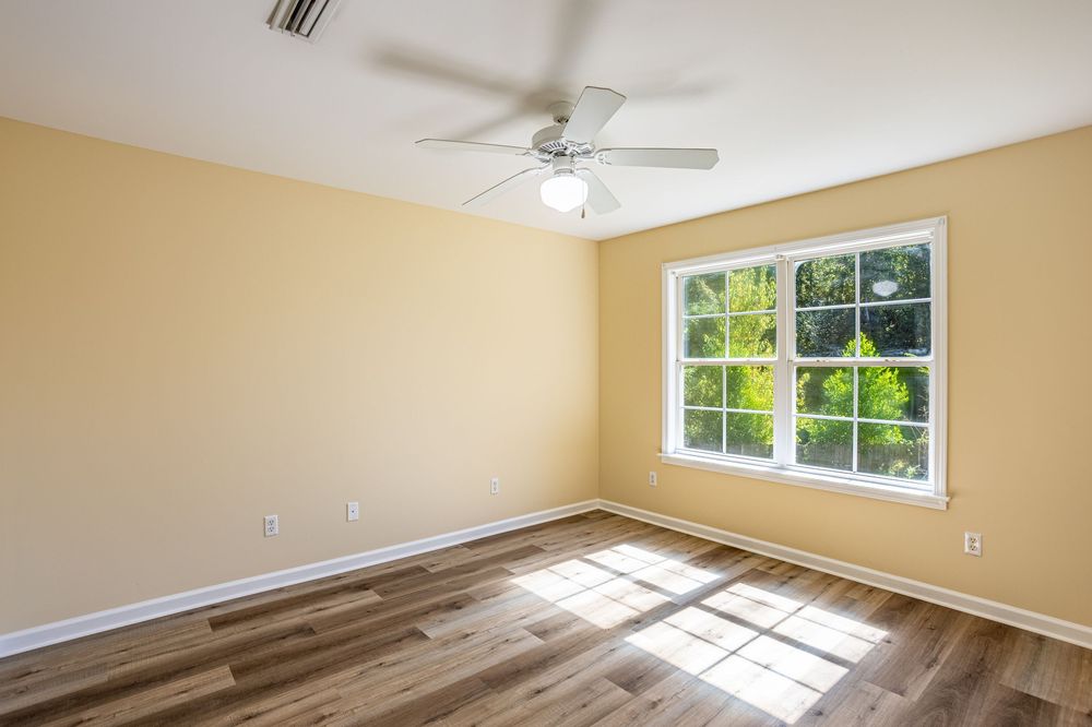Empty room with beige walls, ceiling fan, and large windows letting in natural sunlight in Dothan, AL.