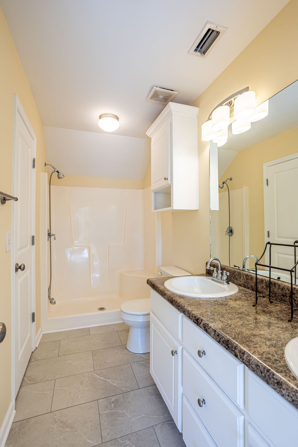 Modern bathroom interior with white vanity, granite countertop, tile floor and glass-enclosed shower in soft yellow tones.