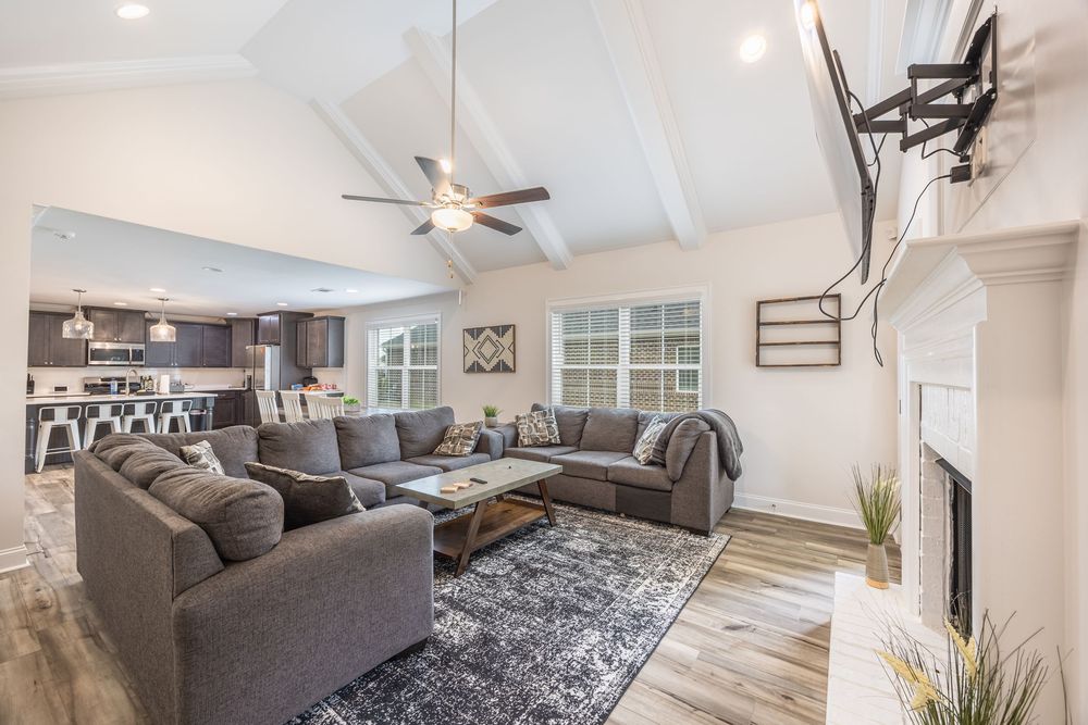 Spacious open-concept living room with vaulted ceiling, gray sectional sofa, hardwood floors, fireplace, and modern ceiling fan.