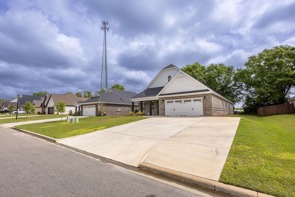 Single-story suburban home with two-car garage, concrete driveway, green lawn, and a tall communication tower visible in the background.