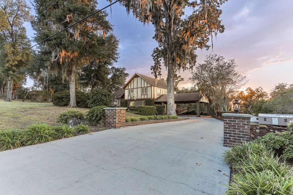 Elegant Tudor-style home with stone accents and landscaping viewed from curved driveway at sunset in Marianna, FL.