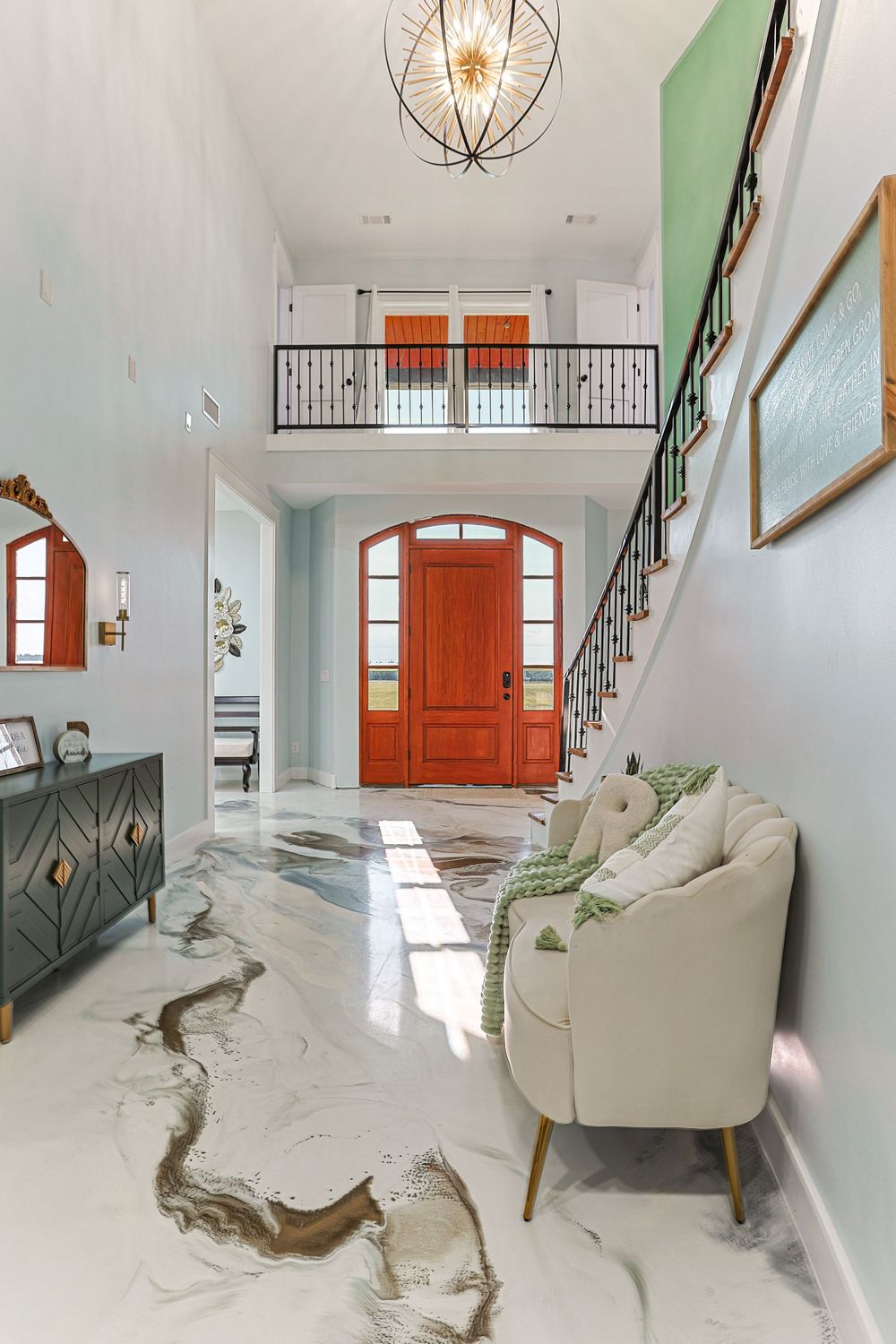 Modern entryway with white marble floors, bright orange door, and geometric pendant light fixture in a minimalist design in Taylor, AL.