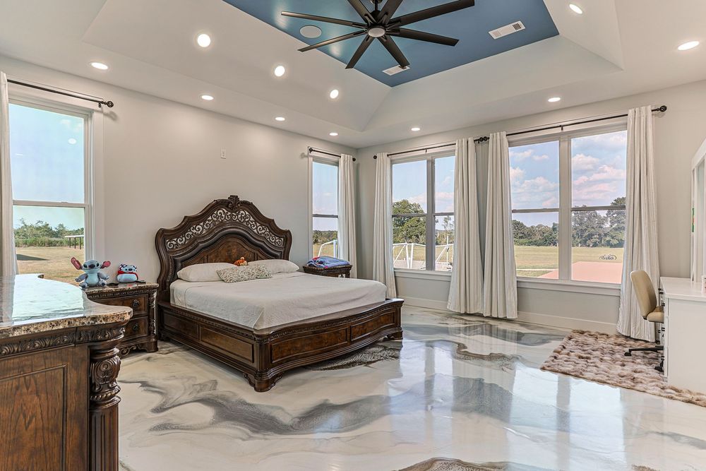 Modern master bedroom with panoramic windows, ornate dark wood bed frame, and ceiling fan in luxury home interior in Taylor, AL.