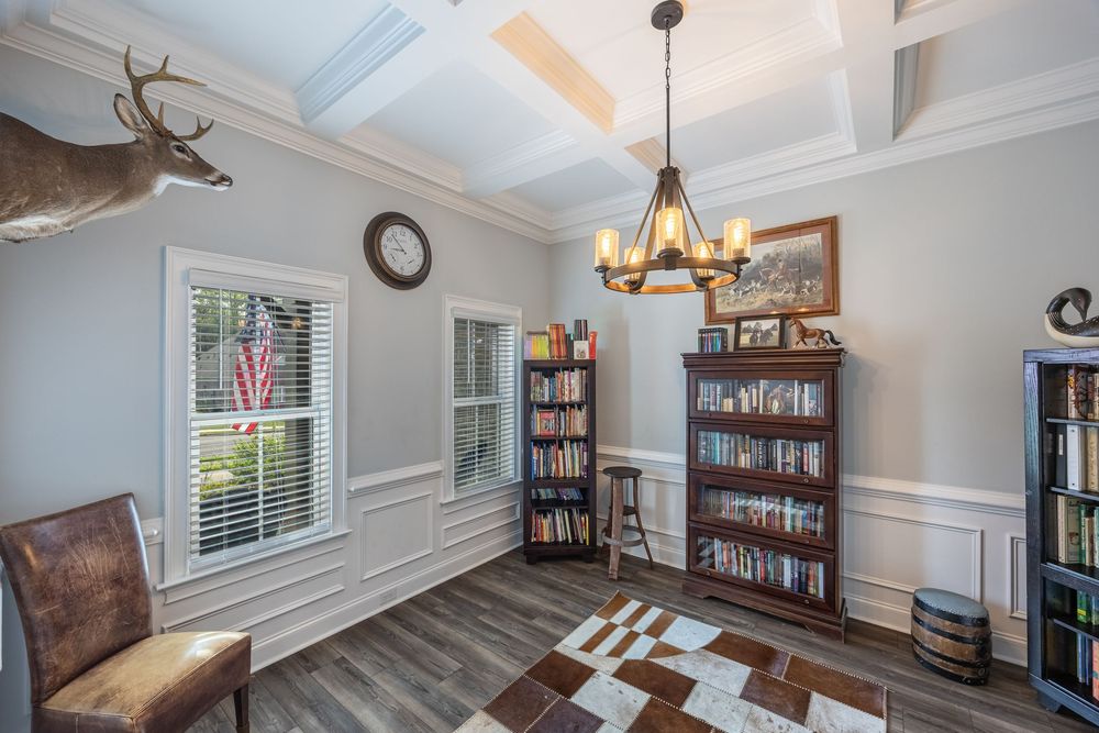 Elegant study with coffered ceiling, chandelier, built-in bookshelves, wainscoting, hardwood floors, and mounted deer head decor.