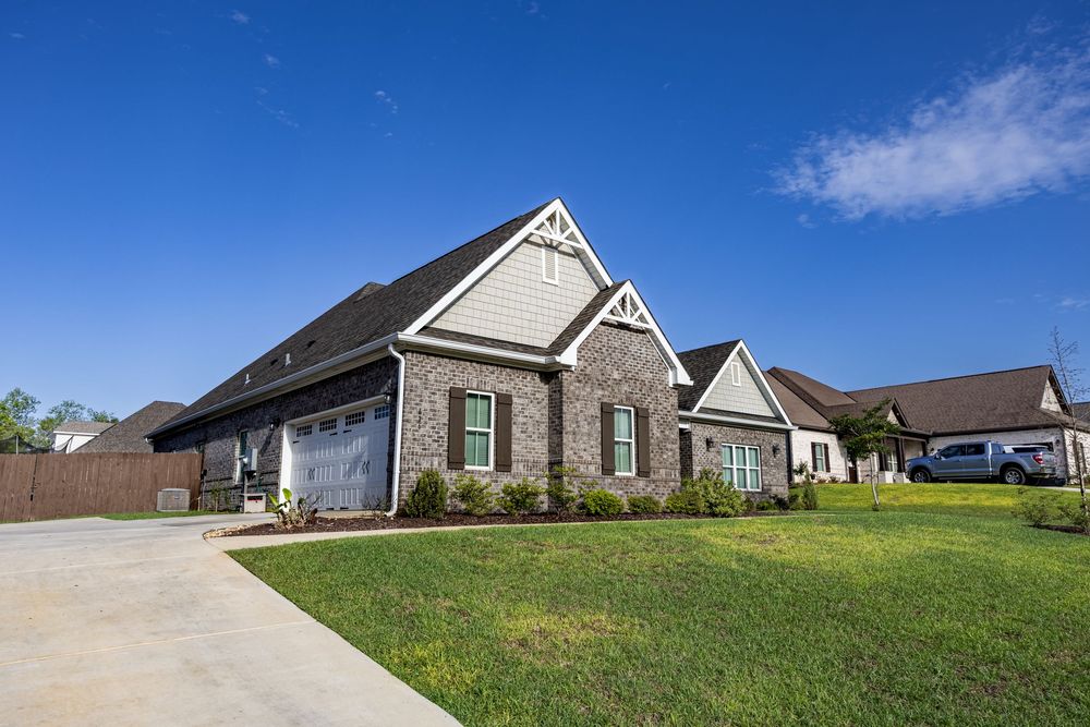 A charming brick and siding craftsman-style home with a two-car garage, lush green lawn, and blue skies in a suburban neighborhood.