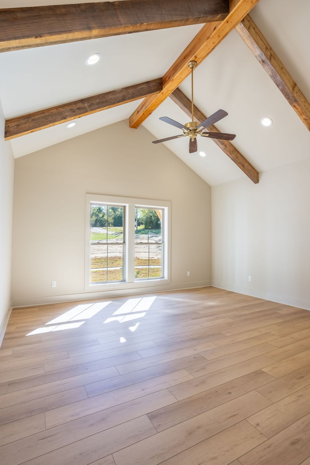 Modern space with exposed wooden beams, white walls, and light hardwood flooring showcases vaulted ceilings and natural light in Ozark, AL.