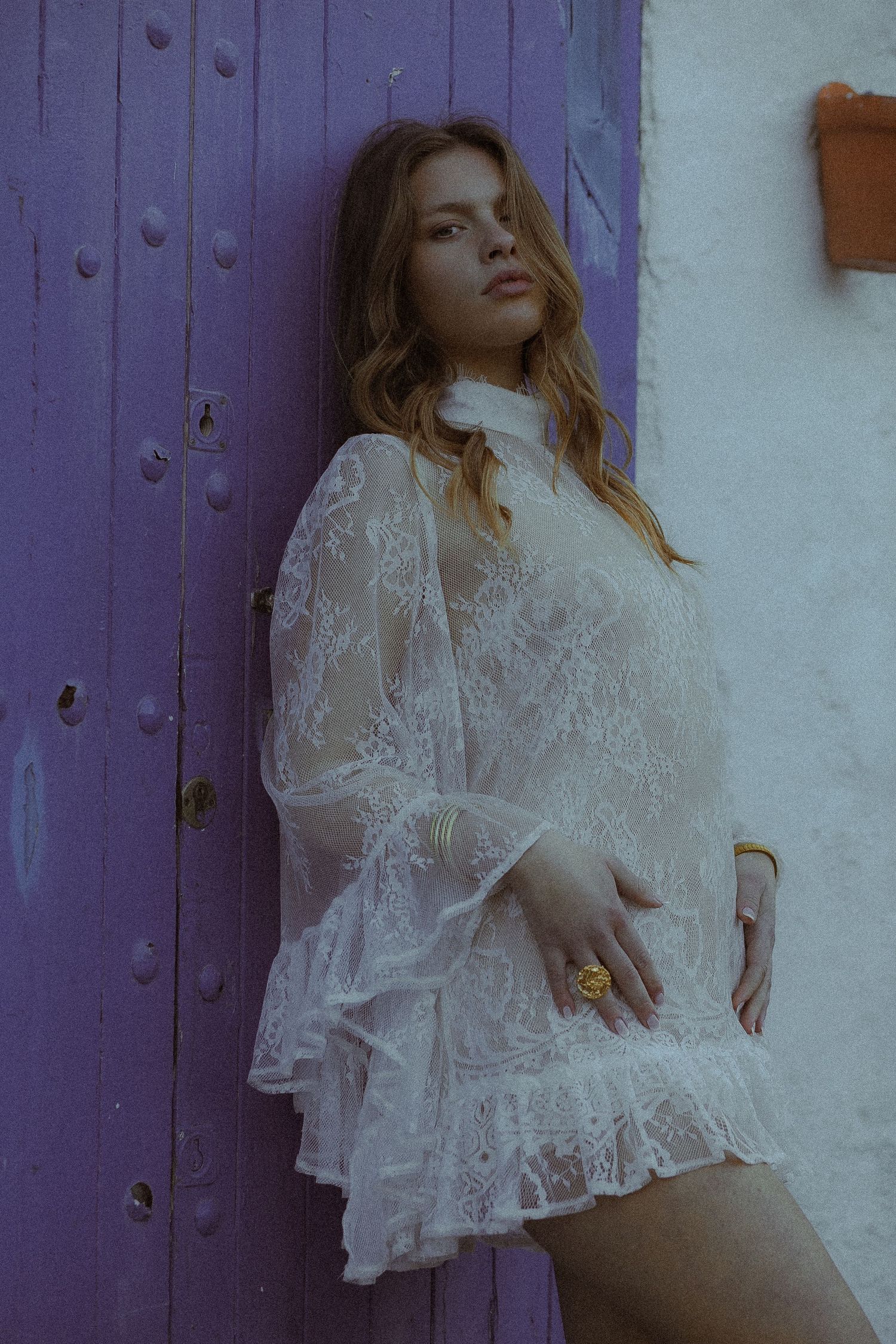 Artistic fashion photos featuring a sheer white lace blouse against a purple wall.