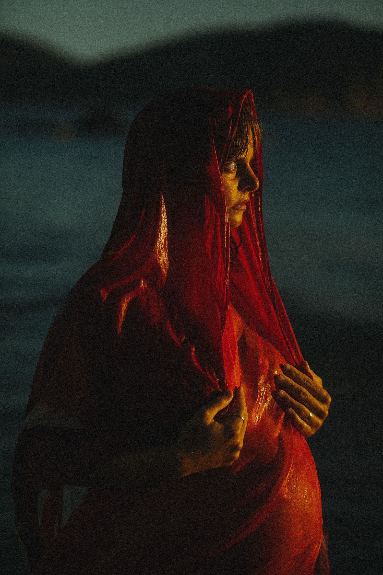 Dramatic red lighting illuminates a figure draped in flowing fabric.