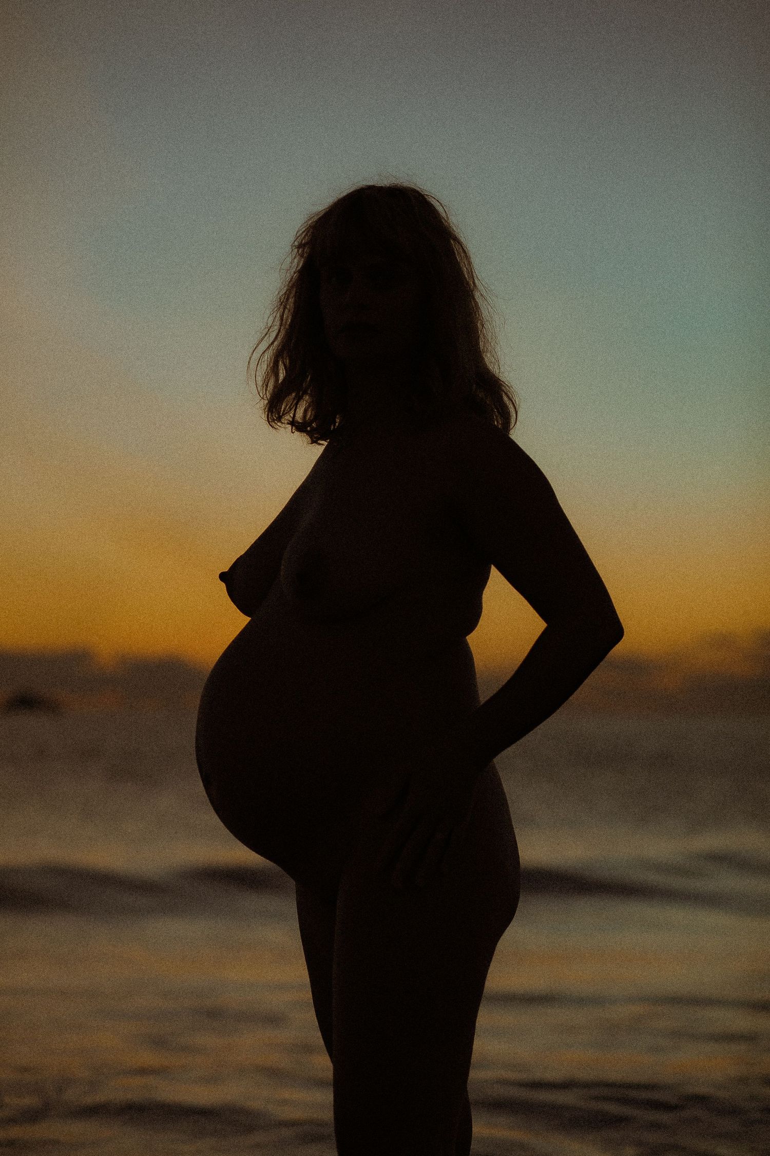 Silhouette figure stands against vibrant sunset sky at beach with dramatic lighting.