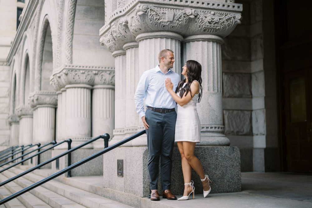 A couple stands close together near ornate stone columns of a historic building during a romantic outdoor moment.