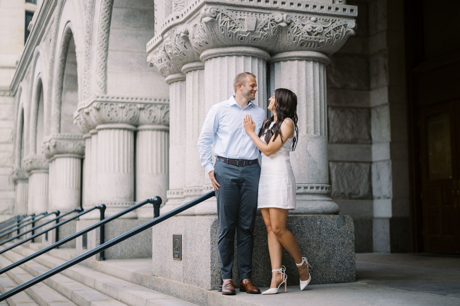 A couple stands close together near ornate stone columns of a historic building during a romantic outdoor moment.