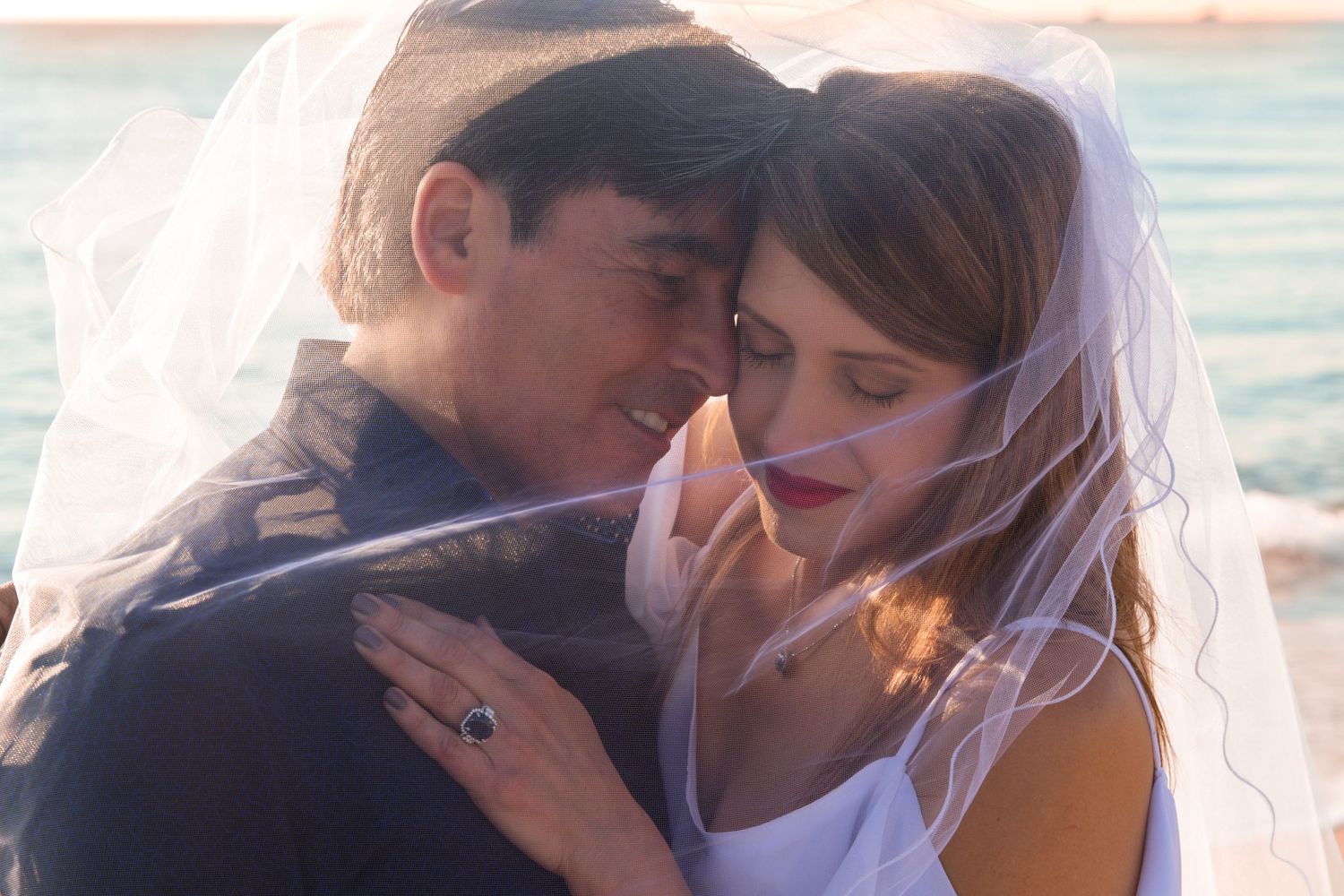Wedding couple sharing intimate moment under bridal veil.