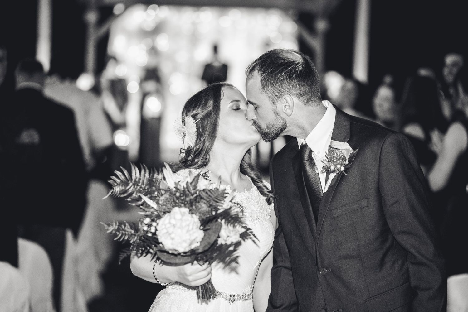Black and white photograph of newlyweds sharing a gentle kiss while holding a beautiful floral bouquet.