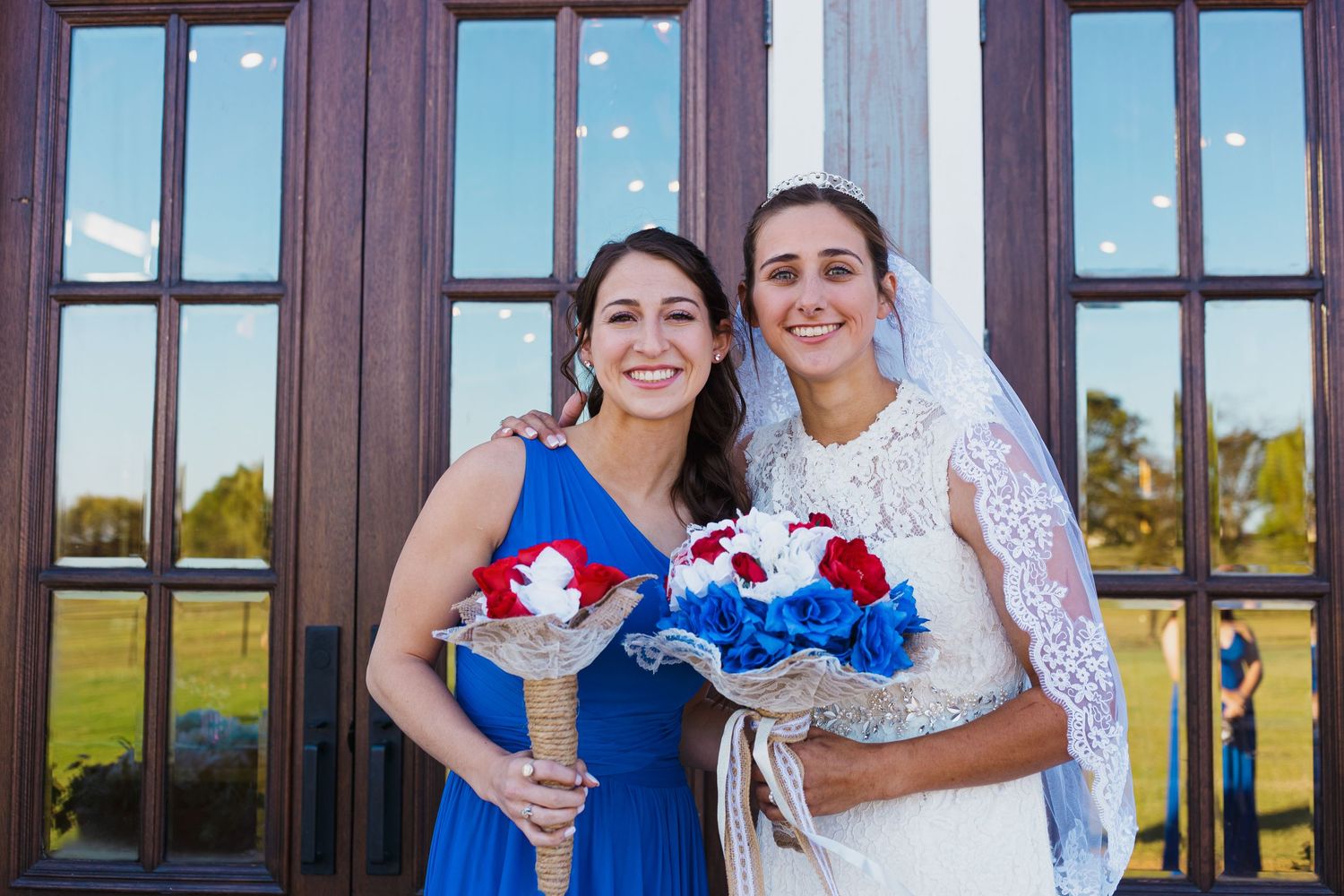 Wedding attendees in blue and white dresses hold coordinated red, white and blue bouquets outside wooden doors. Denison North Texas Wedding