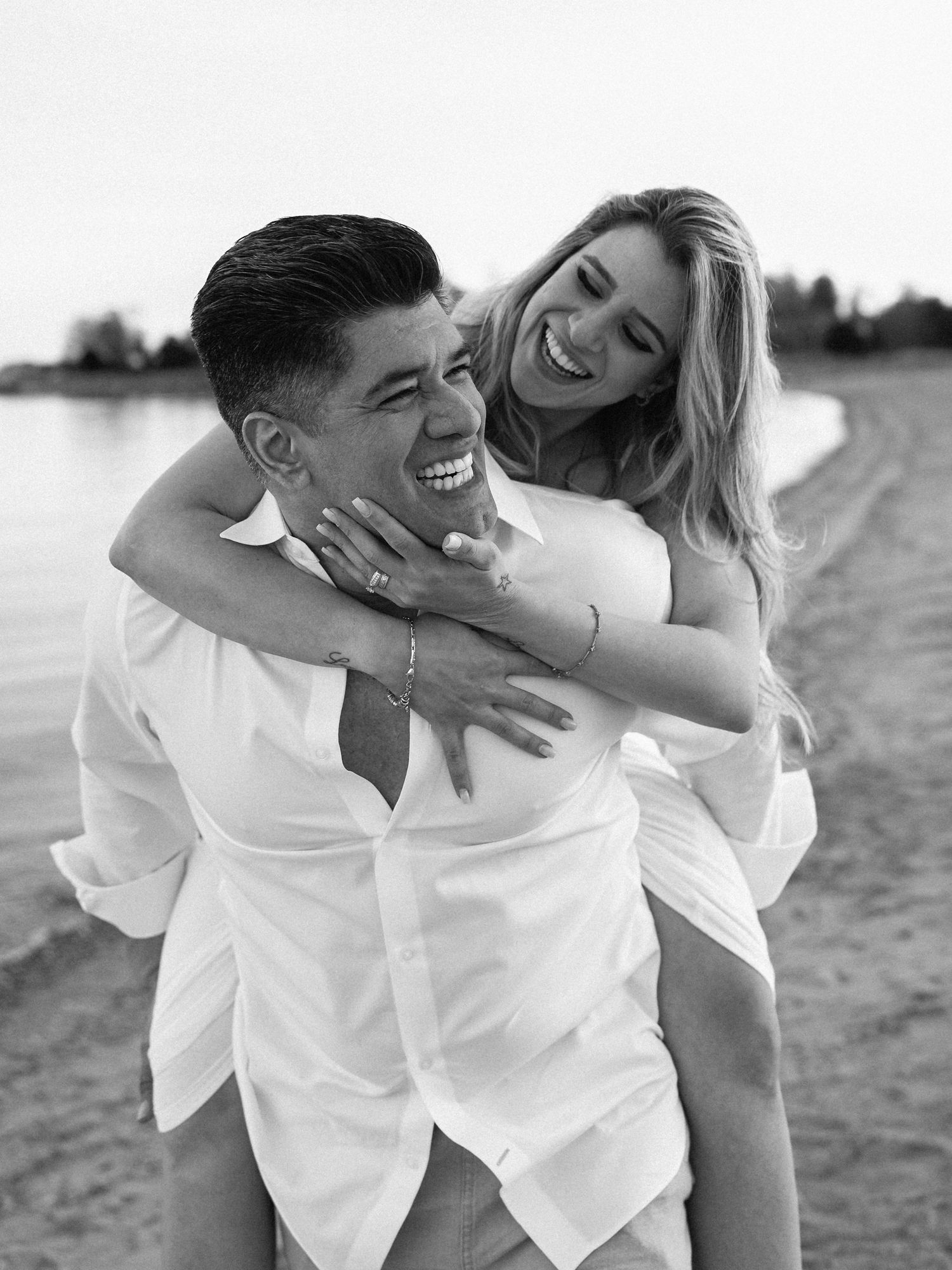 Candid black and white photo of a joyful couple embracing on the beach.