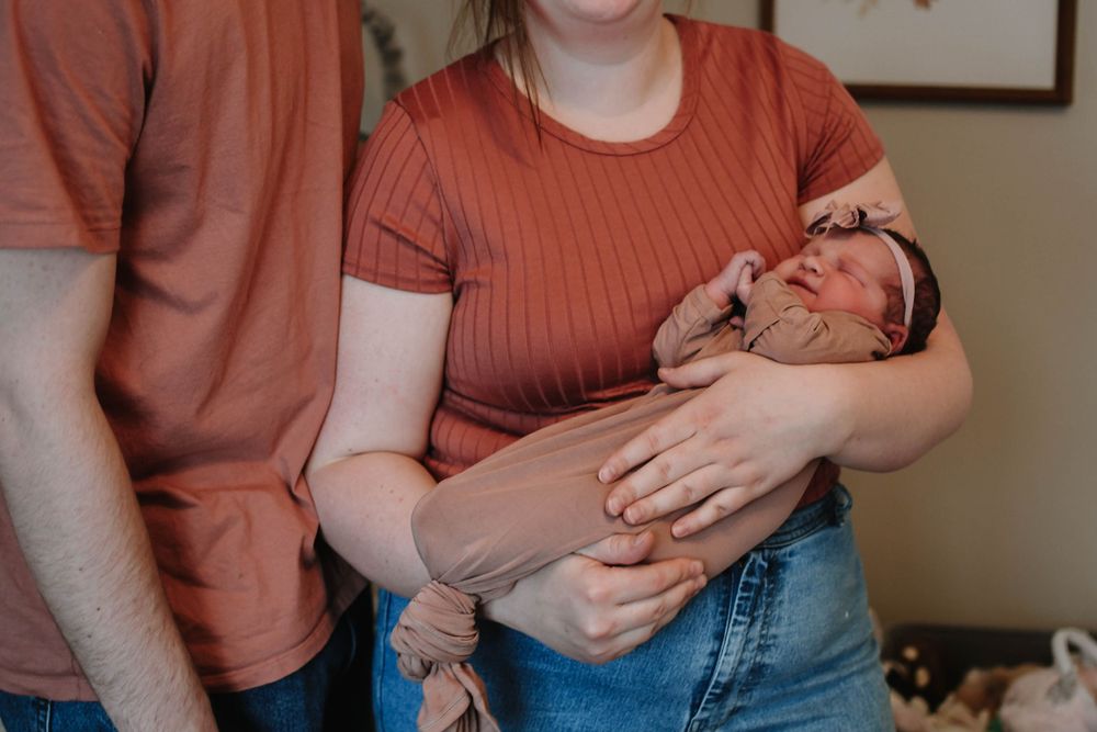 A newborn baby sleeps peacefully while being cradled in rustic home setting.