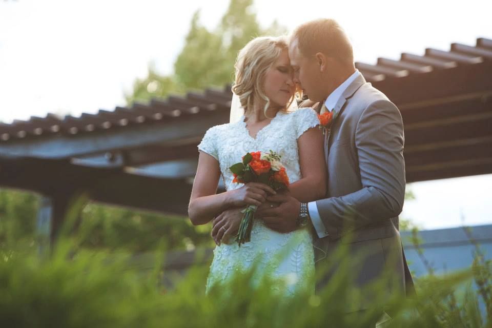 Intimate moment between couple with coral bouquet against natural backdrop.