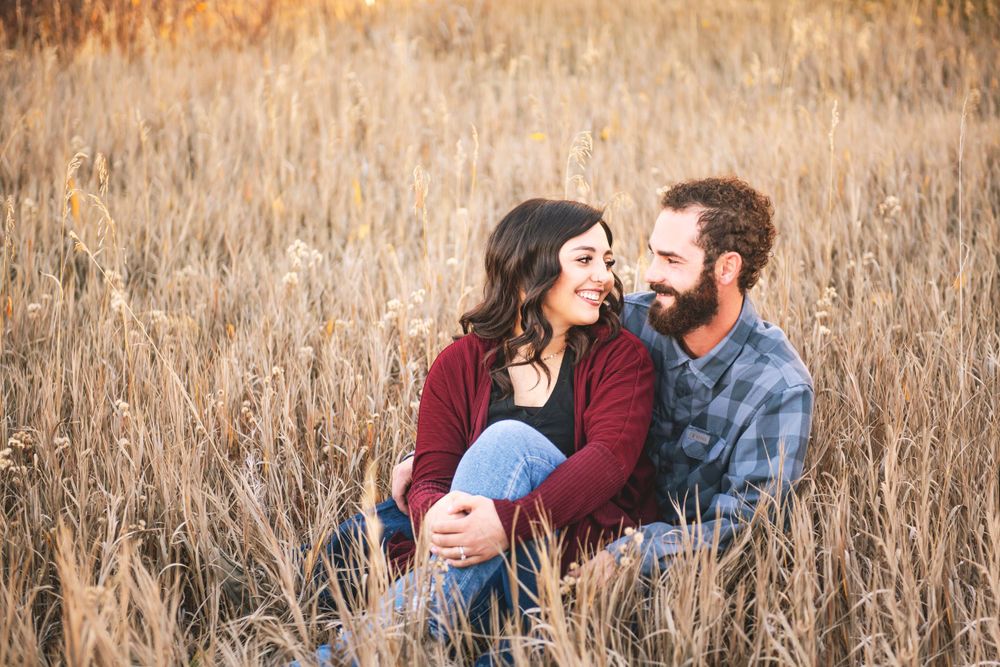 A couple shares a romantic moment while sitting in tall autumn grass.