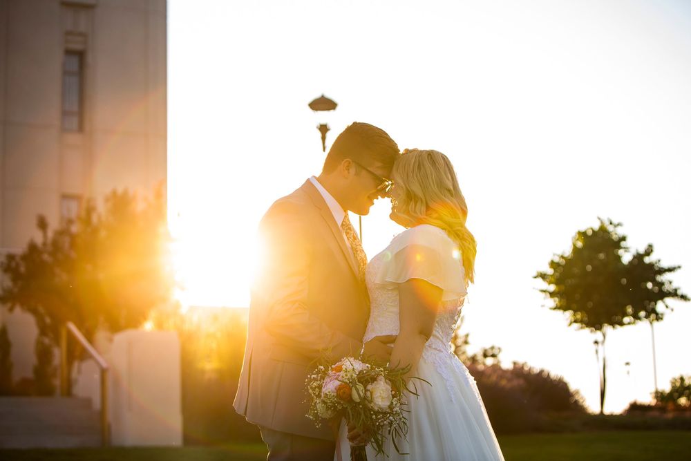 A couple sharing a romantic moment during golden hour sunset with a bouquet of flowers outside a building.