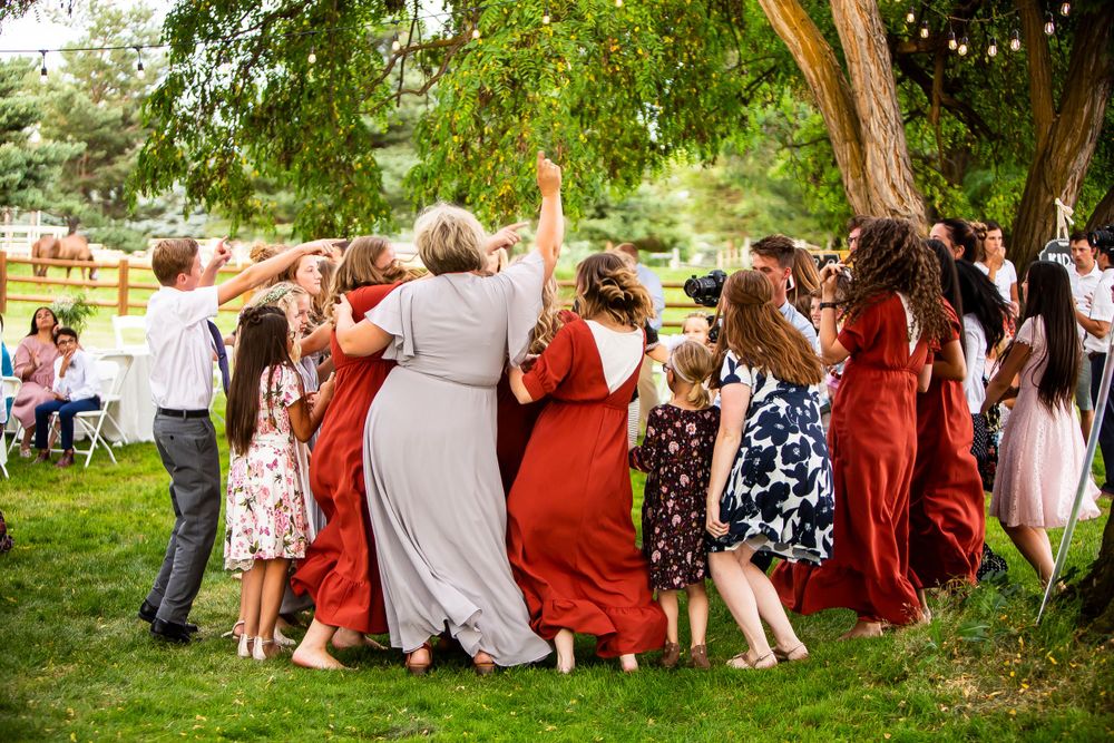 A joyful group dancing in a circle at an outdoor garden party with string lights and trees in the background.