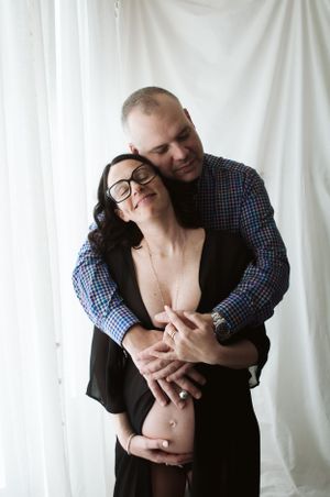 Servizio fotografico di maternità di una coppia intima abbraccianti su sfondo bianco.