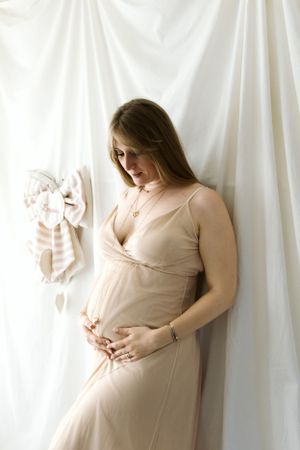 Serie di servizi fotografici artistici di maternità in tenui toni del beige su sfondo di tessuto bianco.