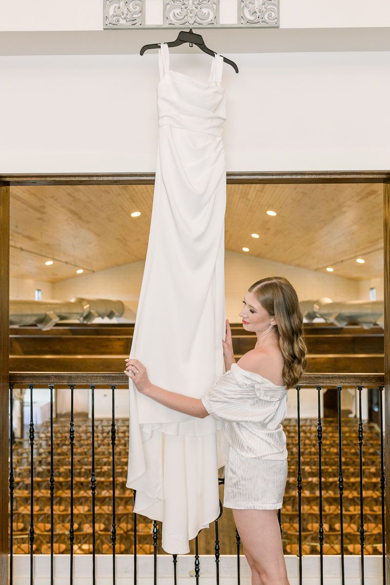 Jenna admires her wedding dress, which hangs from the ceiling at Lilydale