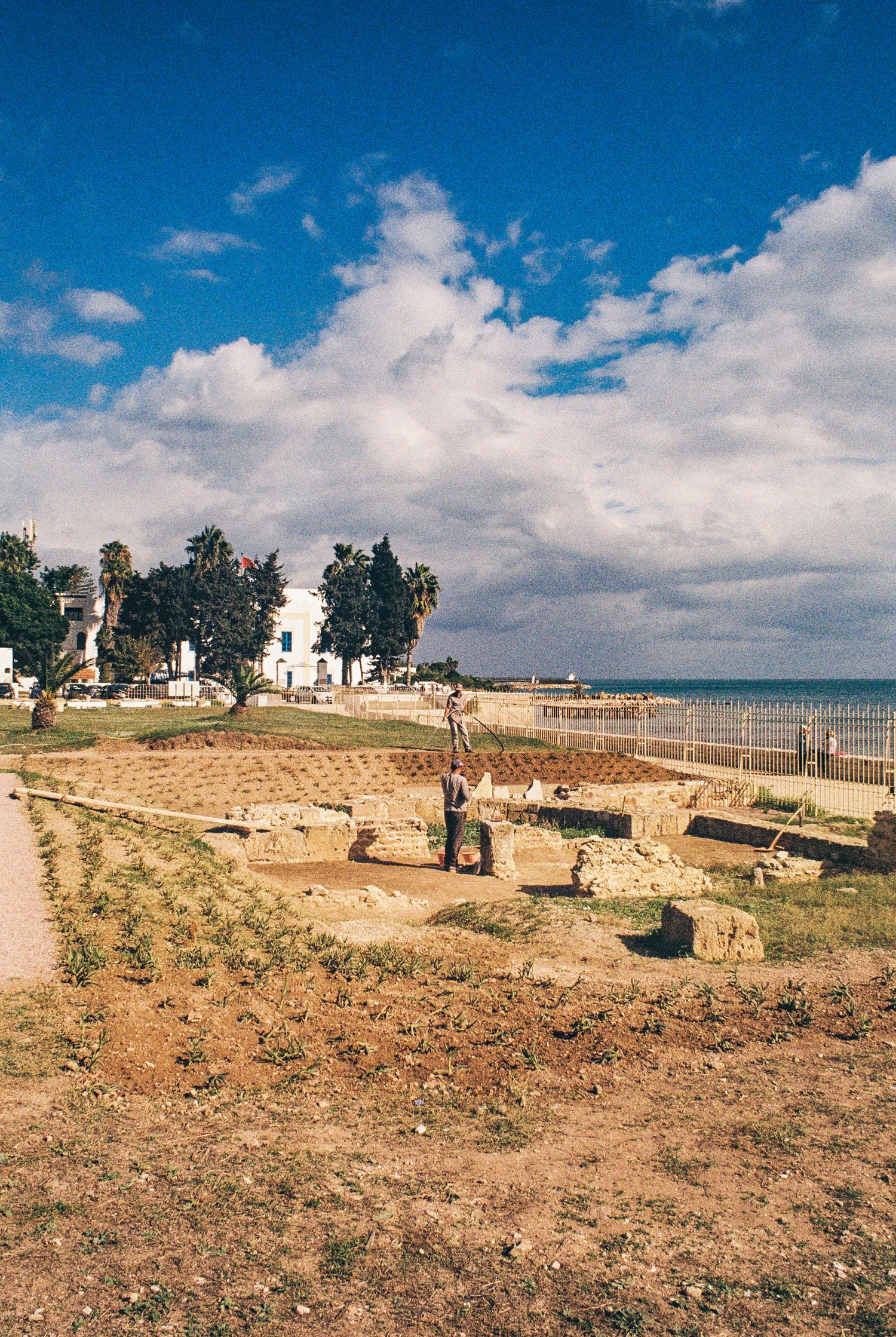 Ancient Roman ruins and archaeological site along Mediterranean coastline with blue sky and white clouds overhead.