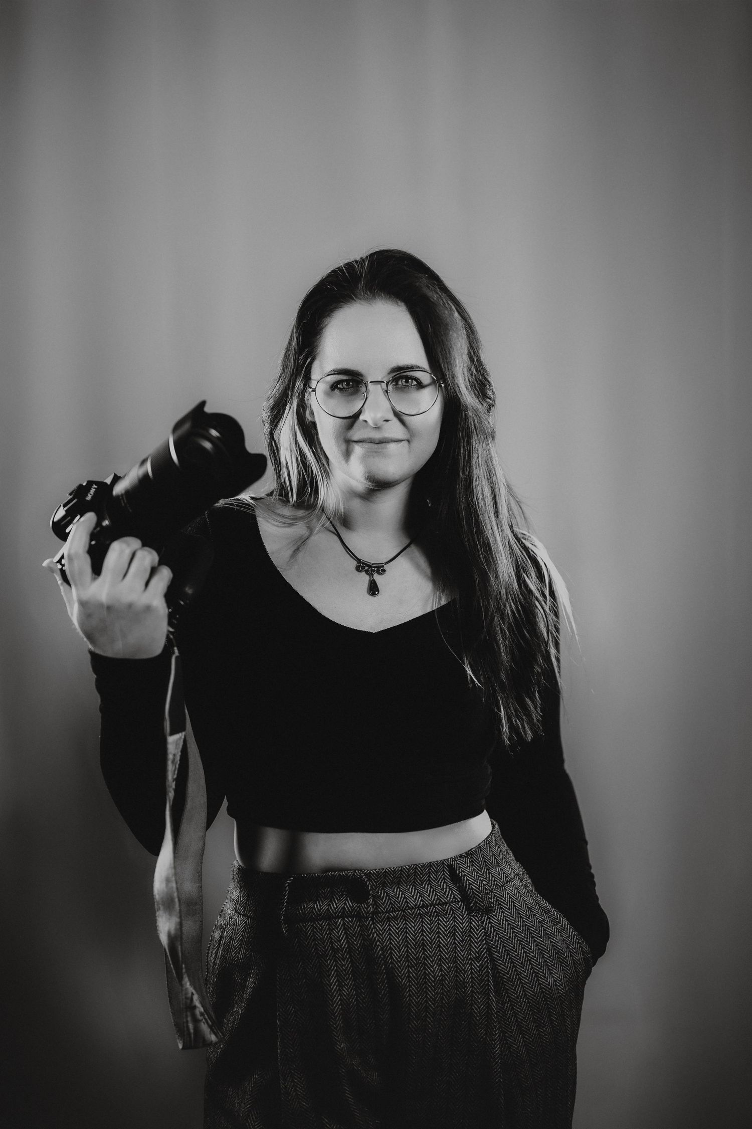 Portrait of a photographer holding a professional camera wearing casual attire in a monochrome setting.