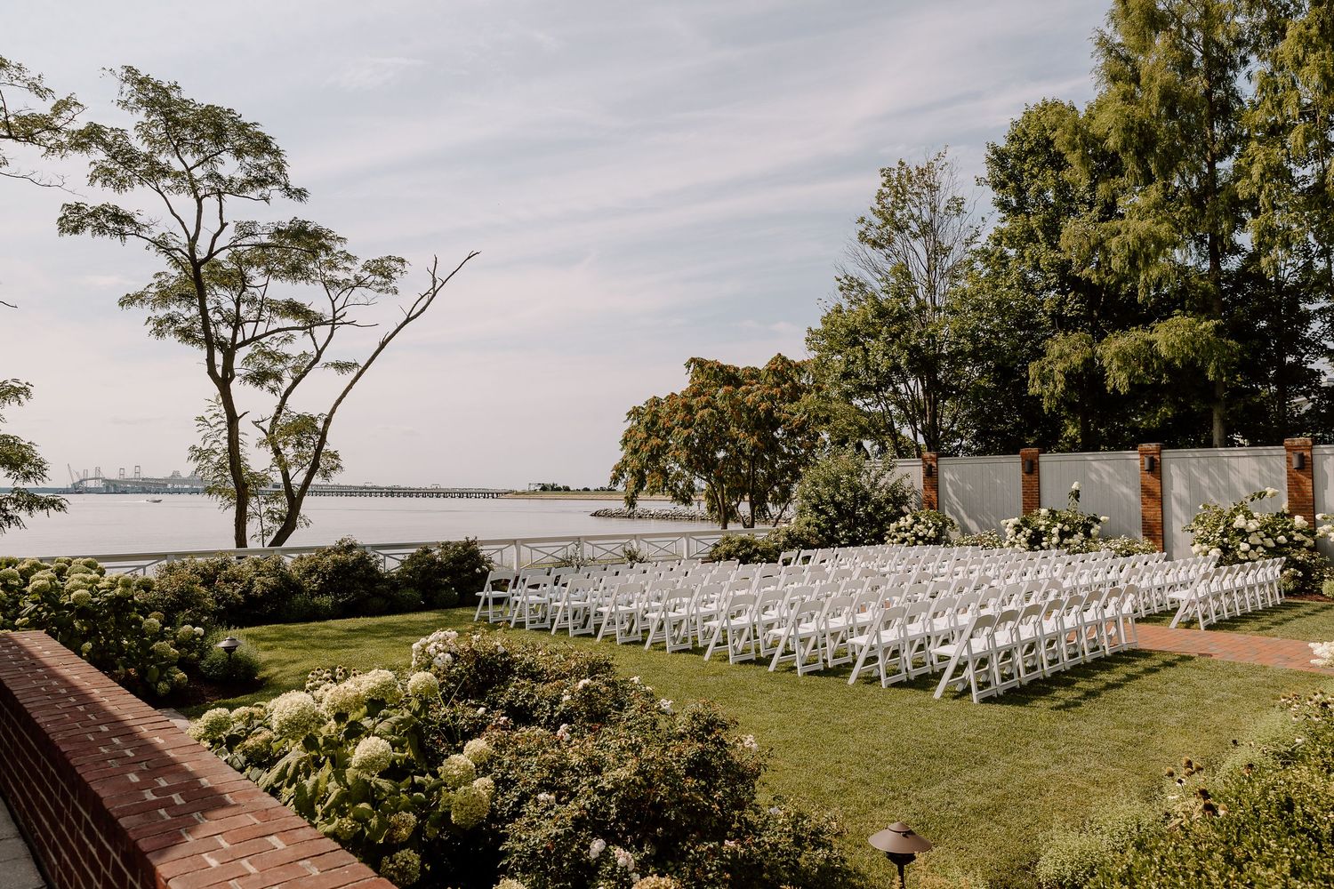 Waterfront wedding ceremony setup with rows of white chairs on a manicured lawn.