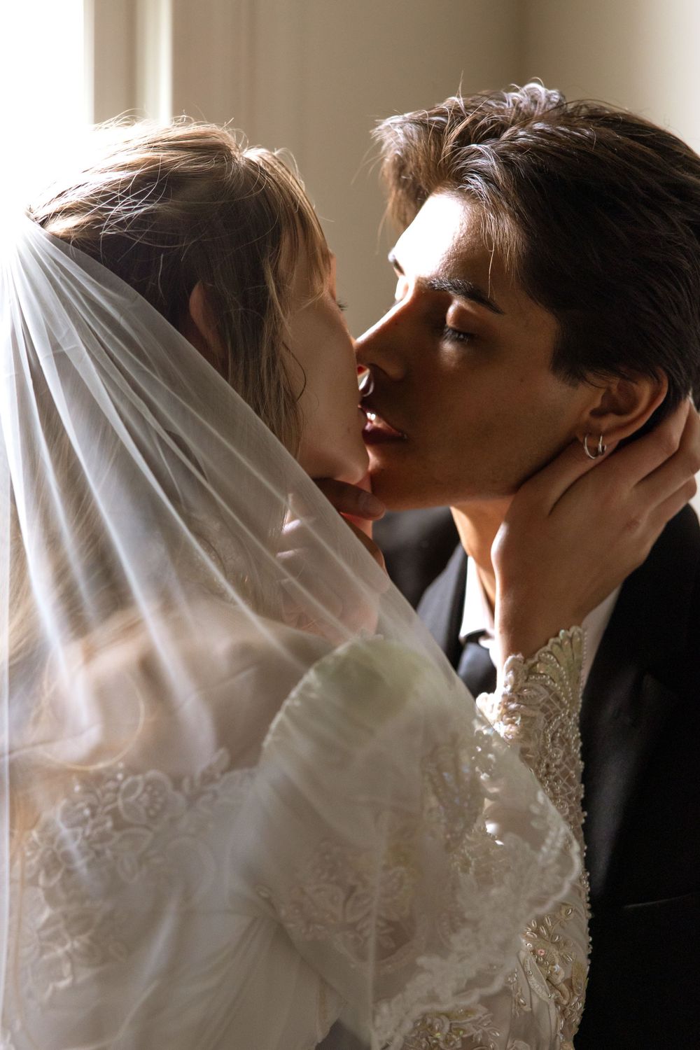 A romantic wedding moment captured in soft light with the bride in a white lace gown and veil sharing a tender kiss.